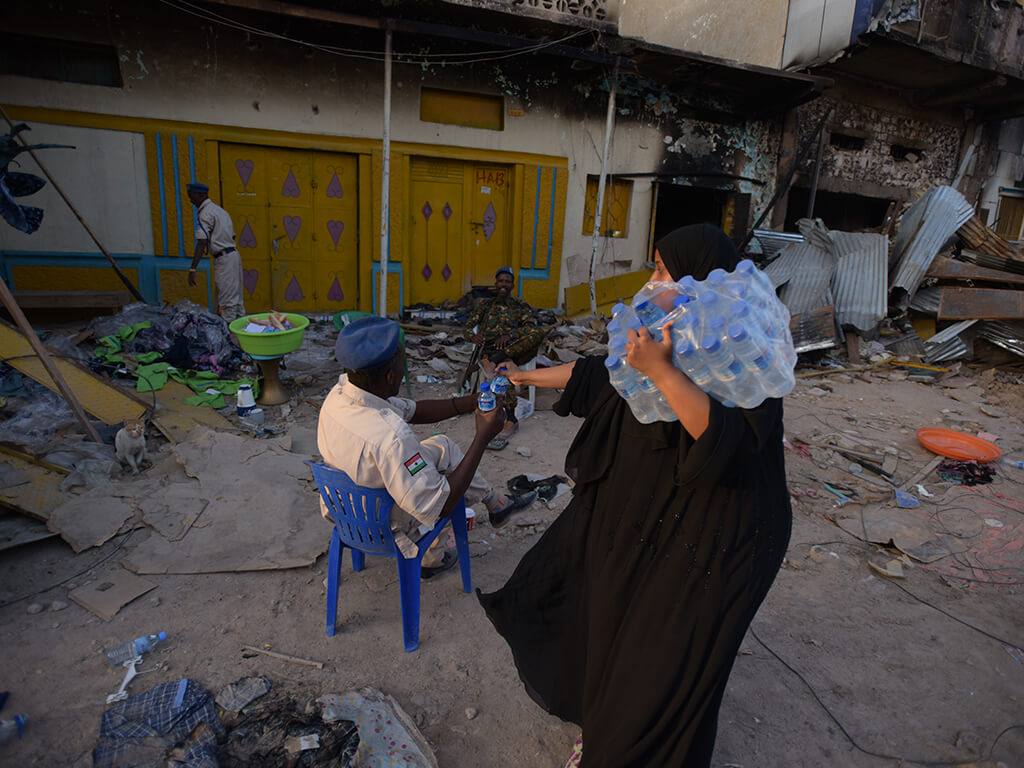 A woman hands a law enforcement officer a bottle of water. Law enforcement were heavily involved in the post- fire period, helping business owners salvage whatever they could from the ruins. PHOTO: Mukhtar Nuur.
